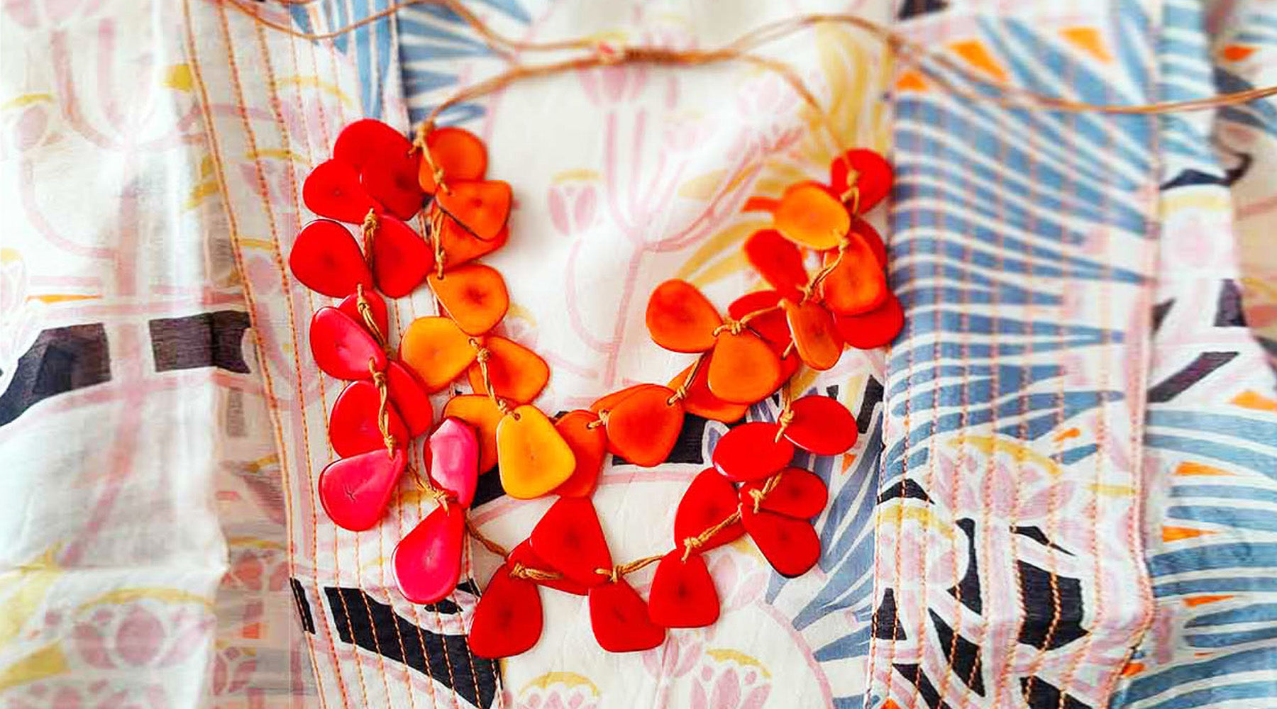 A colourful orange necklace set against a cream and blue background with a leafy print.