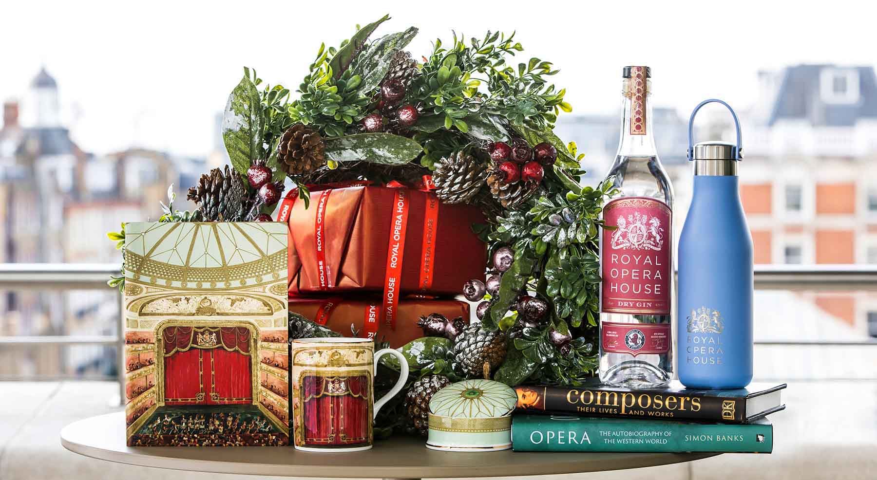 A collection of Royal Opera House souvenirs sitting on a table in front of a stack of wrapped gifts and a festive wreath.